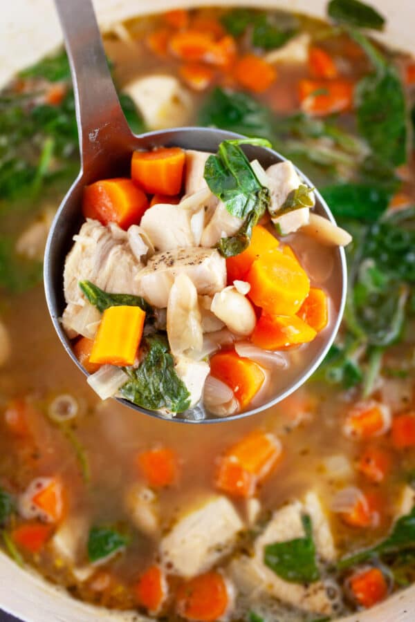Scoop of turkey white bean soup lifted from Dutch oven on metal ladle.