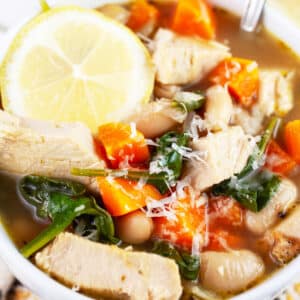 Turkey white bean soup with Parmesan cheese and lemon wheel in white bowl with spoon.