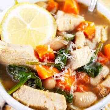 Turkey white bean soup with Parmesan cheese and lemon wheel in white bowl with spoon.