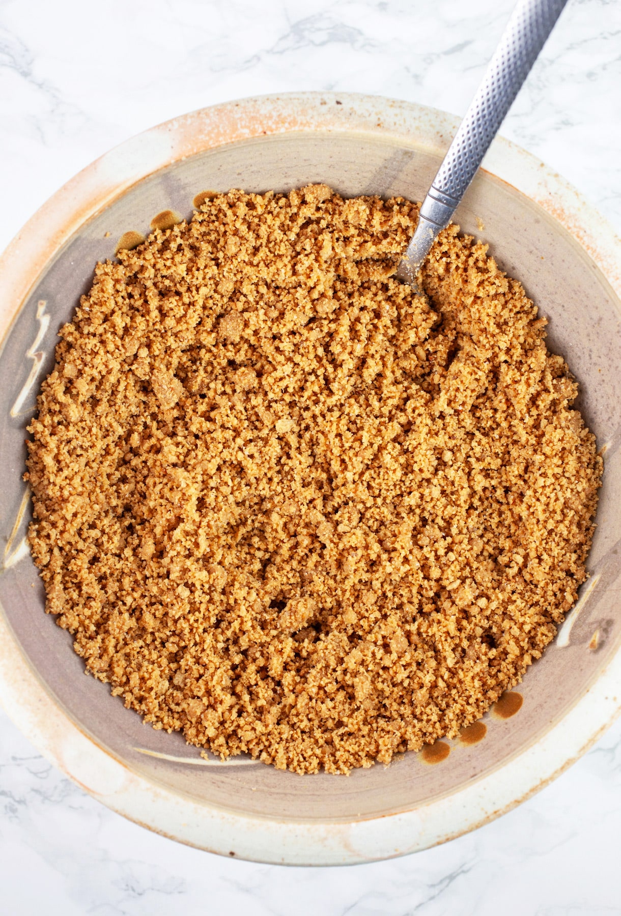 Graham cracker and melted butter mixture in ceramic bowl with spoon.
