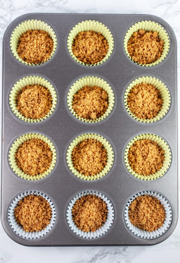 Graham cracker mixture spooned into muffin tin lined with cupcake liners.