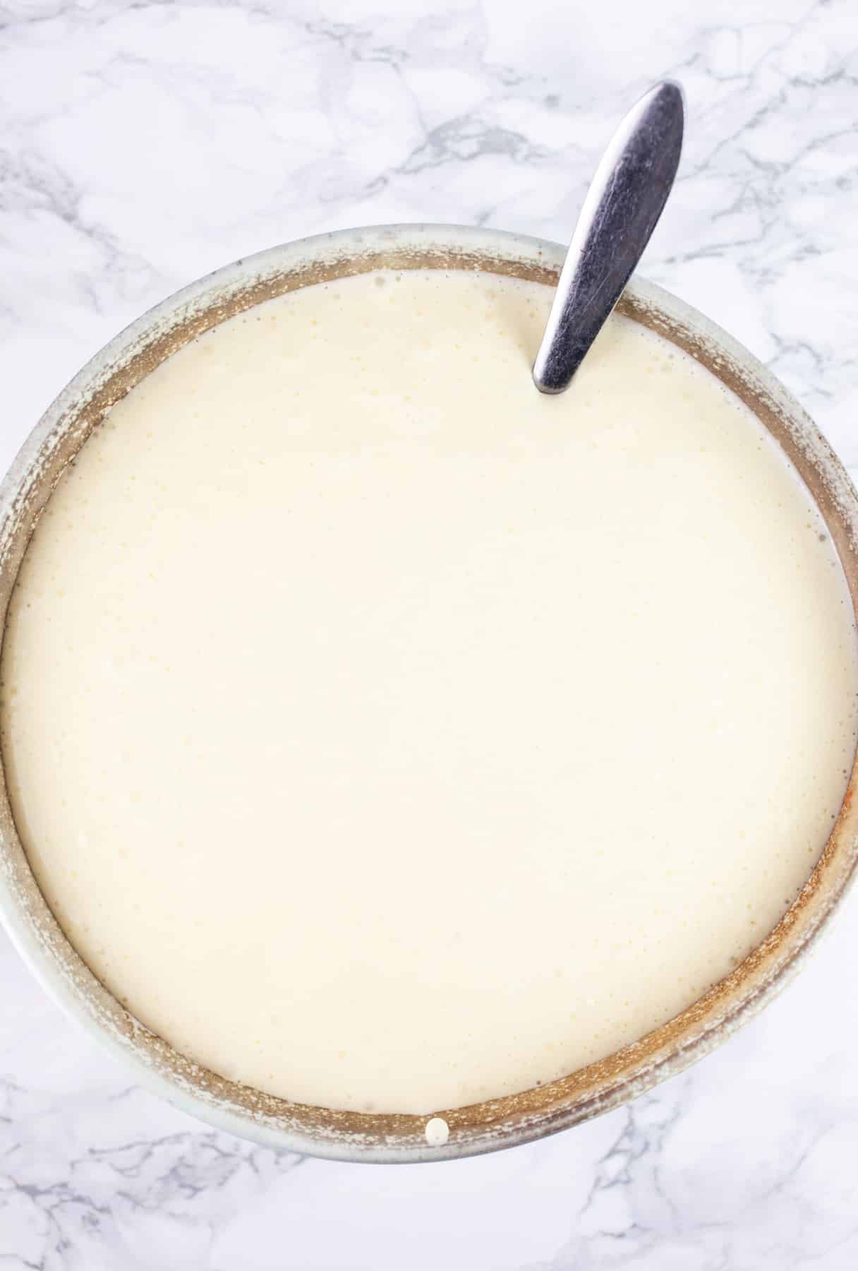 Cheesecake filling mixture in ceramic bowl with spoon.