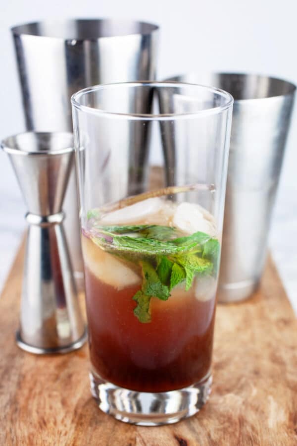 Pomegranate mojito cocktail halfway prepared on wooden cutting board with bar tools.