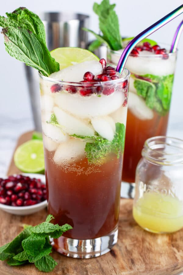 Pomegranate mojito ingredients on wooden serving board with cocktail shaker.
