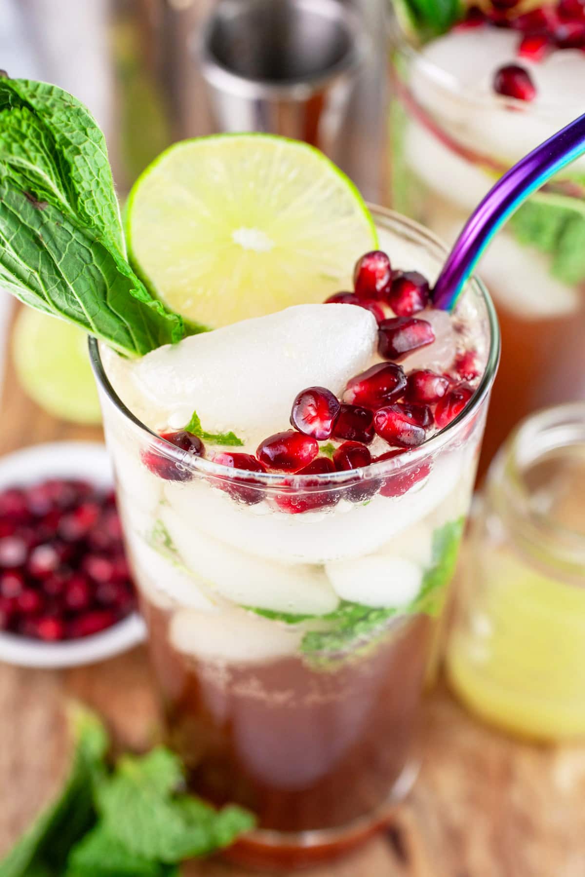 This Pomegranate Mojito Cocktail recipe is one of my favorite holiday cocktails! It's perfect for Christmas and New Year's Eve parties. It's made with rum, lime, and fresh mint. This festive drink is easy to prepare. Leave out the rum for a great mocktail version! #pomegranate #mojito #holidays #christmas Pomegranate mojito cocktail in glass with straw garnished with fresh mint, lime wheel, and pomegranate seeds.
