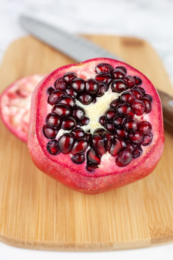 Pomegranate with top removed on wooden cutting board with knife.