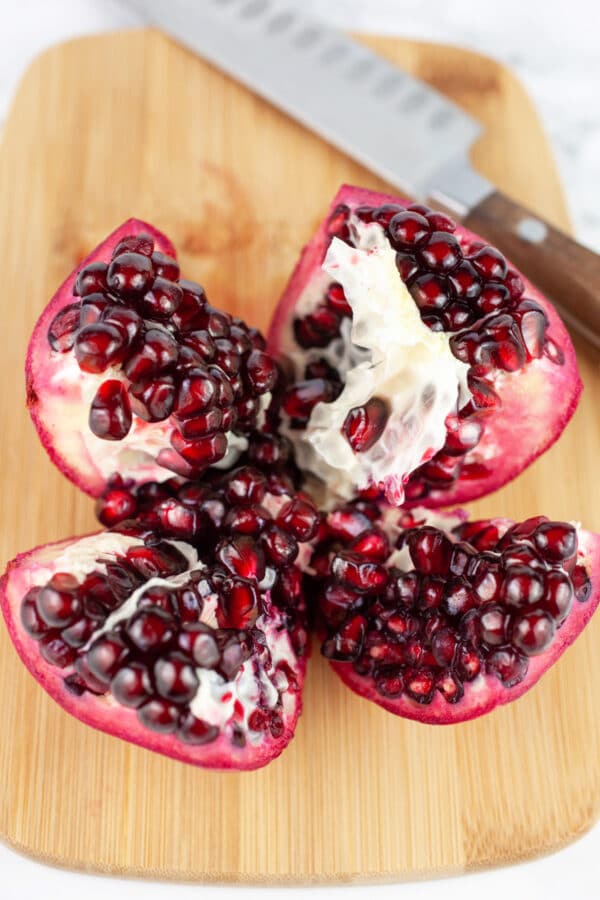 Pomegranate cut into quarters on wooden cutting board with knife.