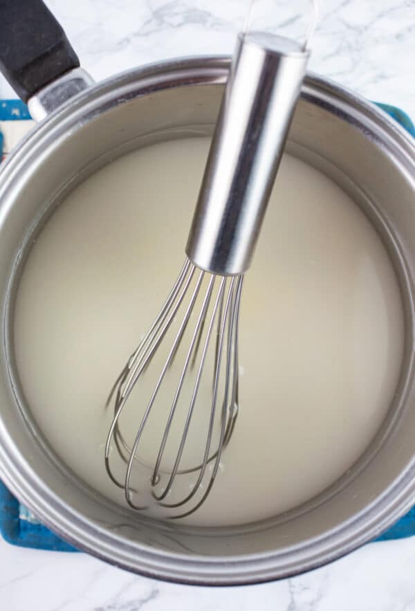 Water and sugar in sauce pan with whisk.