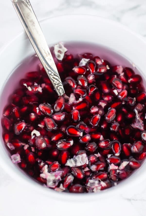 Pomegranate seeds in water in white bowl with spoon.