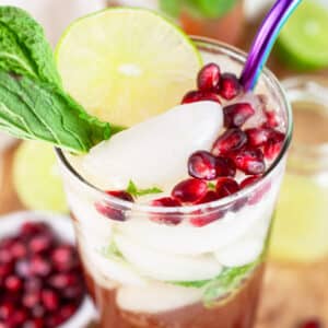 Pomegranate mojito cocktail garnished with fresh mint, lime wheel, and pomegranate seeds.