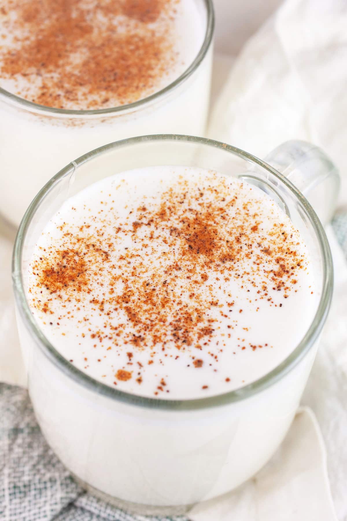 My family makes this Tom and Jerry Holiday Cocktail recipe every year during Christmas! It's an old fashioned drink made with a batter consisting of eggs, milk, rum, and brandy. This Christmas cocktail is warm, boozy, and a little sweet. This easy vintage Tom and Jerry recipe will put you right in the holiday spirit! #christmas #cocktails #holidays #tomandjerry Tom and Jerry cocktails in glass coffee mugs garnished with nutmeg.
