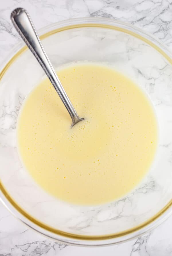 Uncooked Tom and Jerry batter in glass bowl with spoon.