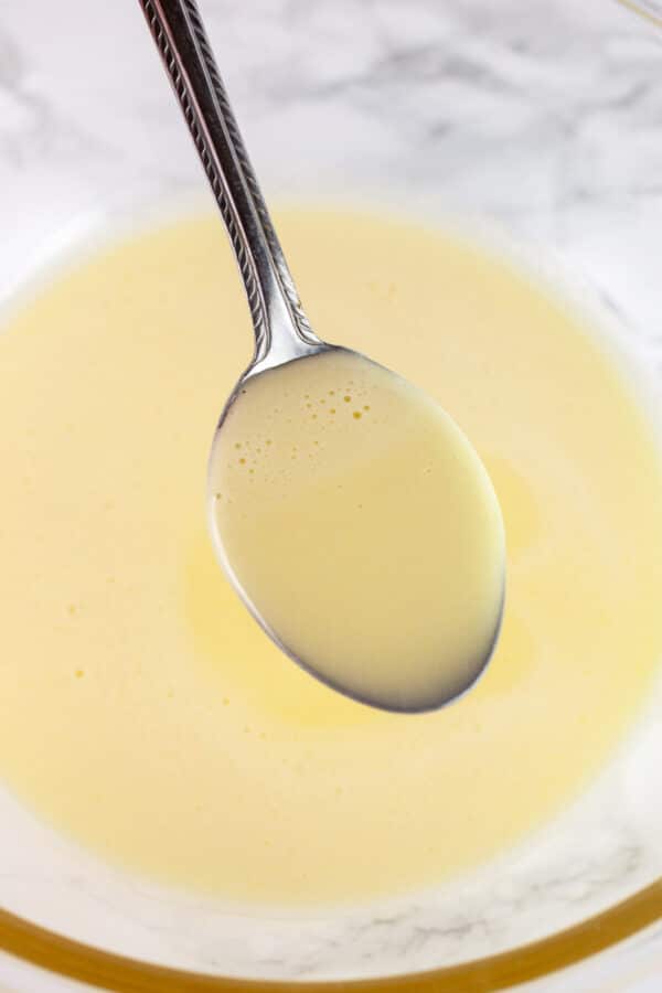 Spoonful of uncooked Tom and Jerry batter lifted from glass bowl with spoon.