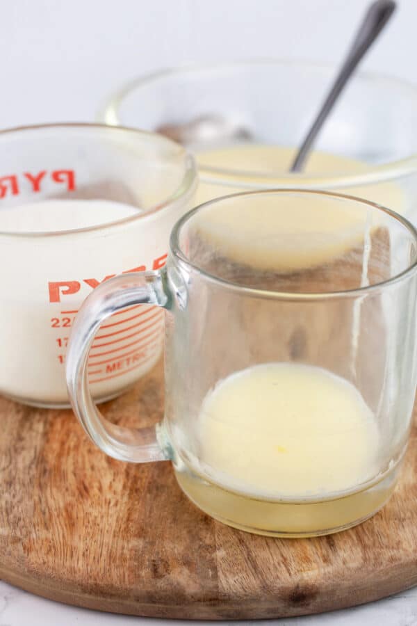 Tom and Jerry batter added to glass coffee cup, warmed milk, and bowl of batter on wooden serving tray.