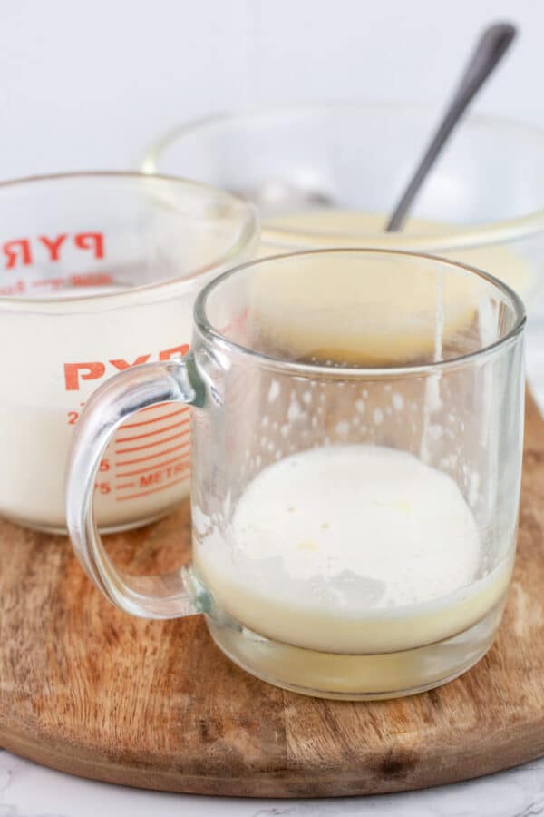 Tom and Jerry batter and warmed milk added to glass coffee mug and bowl of batter on wooden serving tray.