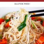 Rice noodles lifted with chopsticks from bowl of Asian chicken soup.