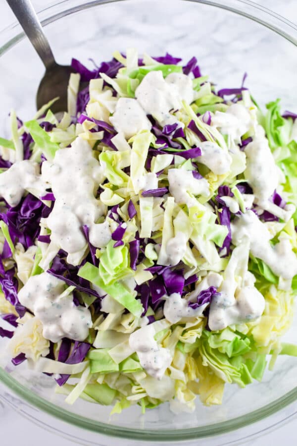 Sliced red and green cabbage in large glass bowl drizzled with blue cheese dressing.