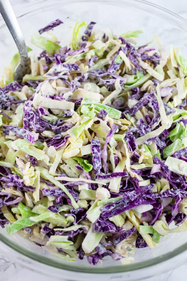 Sliced red and green cabbage in large glass bowl tossed in blue cheese dressing.