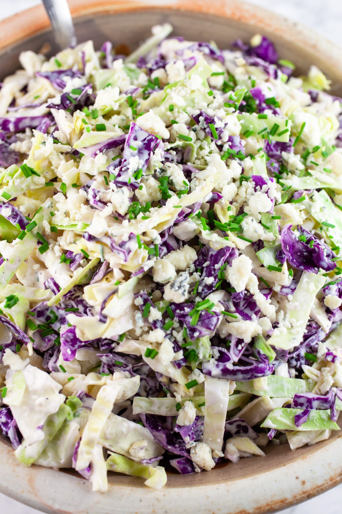 Blue cheese coleslaw garnished with minced chives in ceramic bowl.
