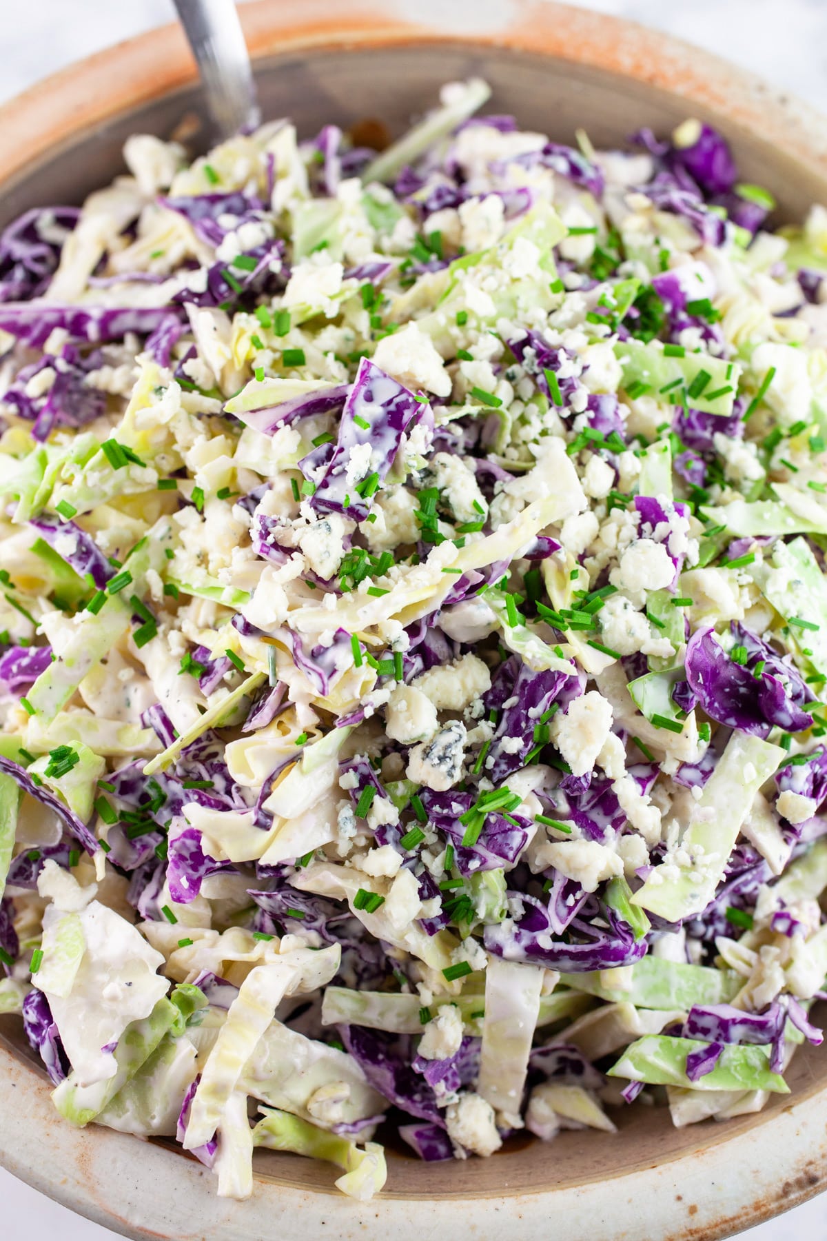Blue cheese coleslaw garnished with minced chives in ceramic bowl.
