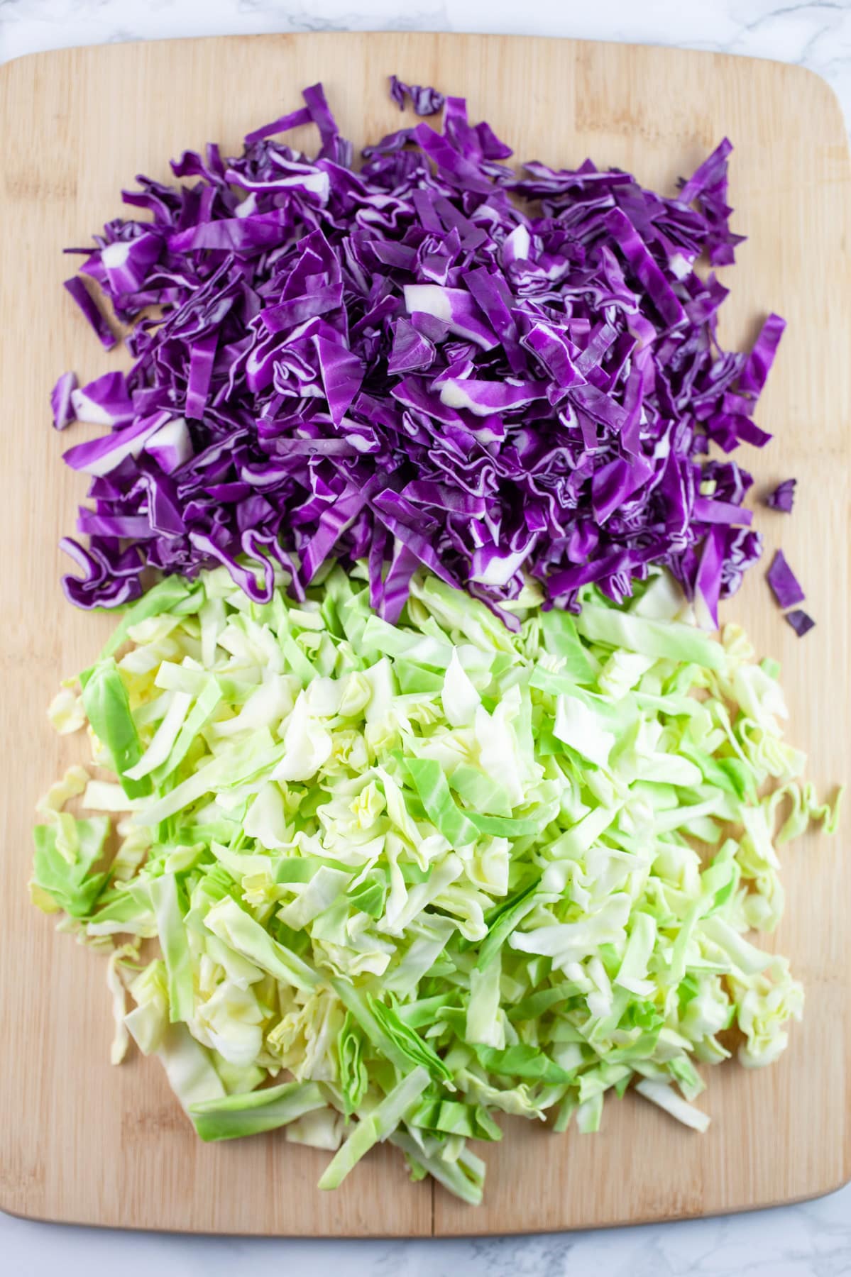Shredded green and red cabbage on wooden cutting board.