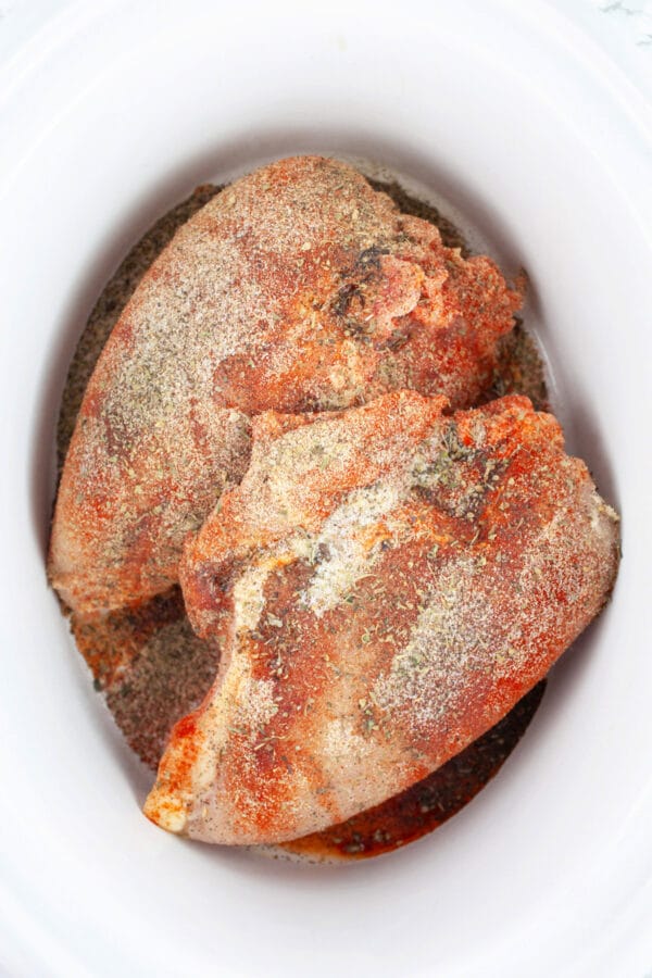 Raw split chicken breasts with spices in slow cooker.