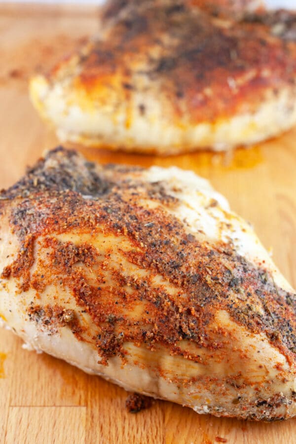 Cooked split chicken breasts on wooden cutting board.