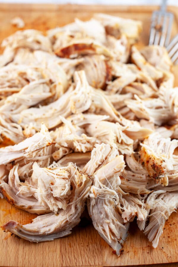 Cooked, shredded chicken breasts on wooden cutting board.
