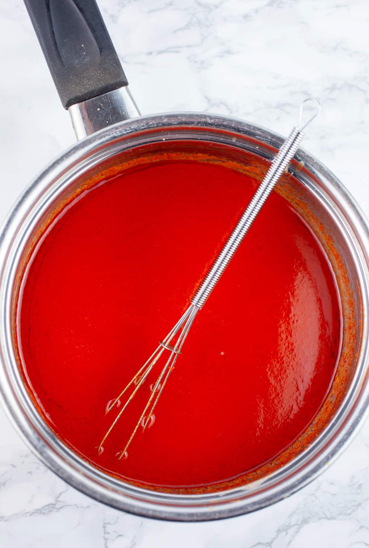 Buffalo sauce in sauce pan with small whisk.
