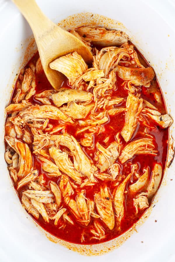 Shredded chicken breasts in buffalo sauce in slow cooker.
