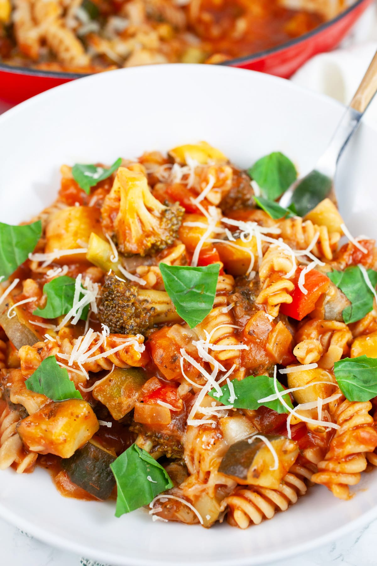One pot veggie pasta garnished with fresh basil in white bowl with fork.