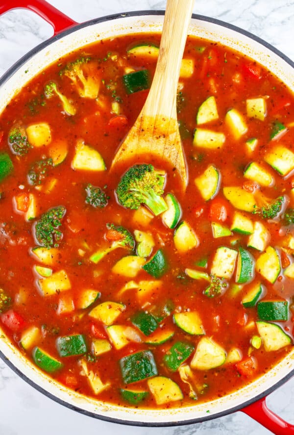 Sauteed vegetables with marinara sauce in skillet with wooden spoon.