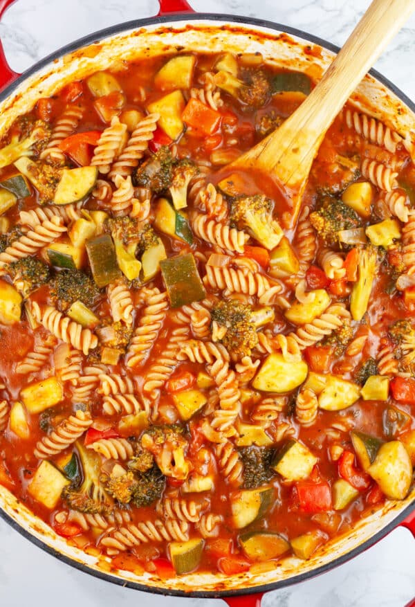 Cooked veggie pasta with marinara sauce in skillet with wooden spoon.