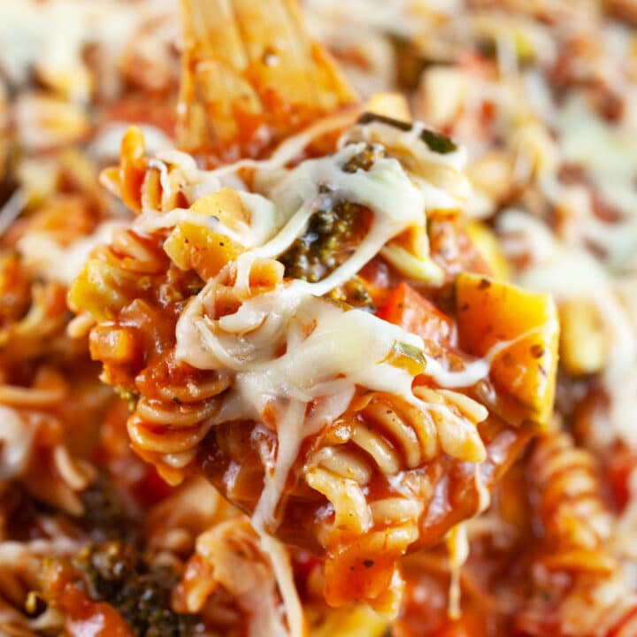 Scoop of cheesy veggie pasta lifted from Dutch oven on wooden spoon.