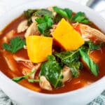 Chicken kale sweet potato soup in white bowl garnished with fresh parsley.