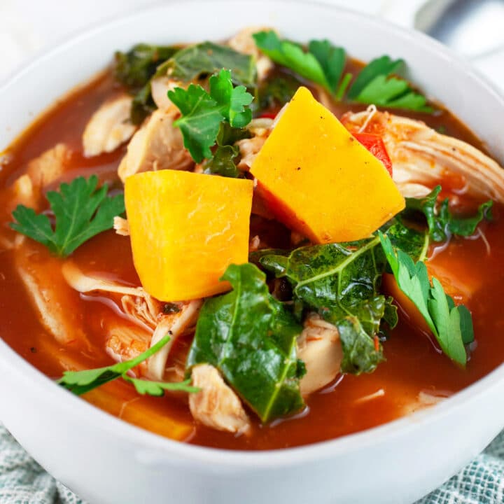 Chicken kale sweet potato soup in white bowl garnished with fresh parsley.