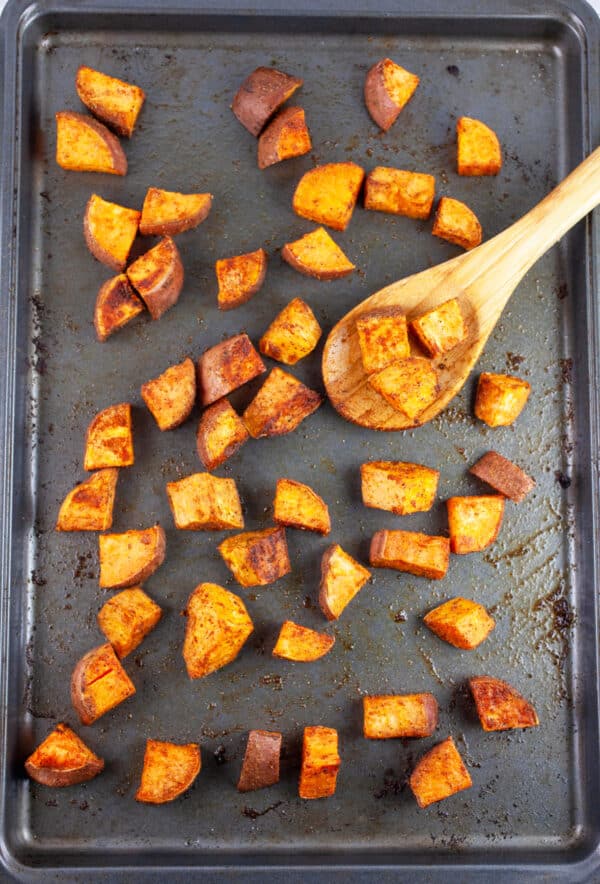Roasted chopped sweet potatoes on baking sheet with wooden spoon.