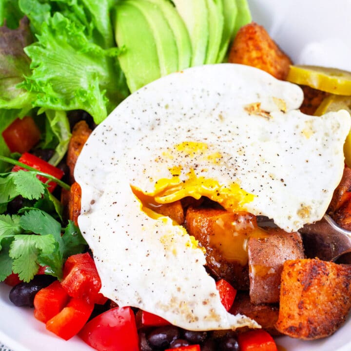 Sweet potato breakfast bowls with fried egg cut open with fork in white bowl.