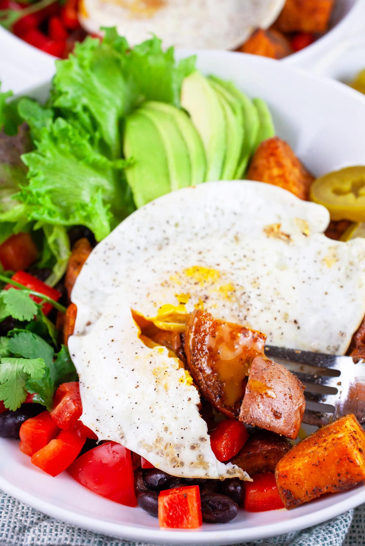 Sweet potato breakfast bowls topped with fried egg cut half with a fork.