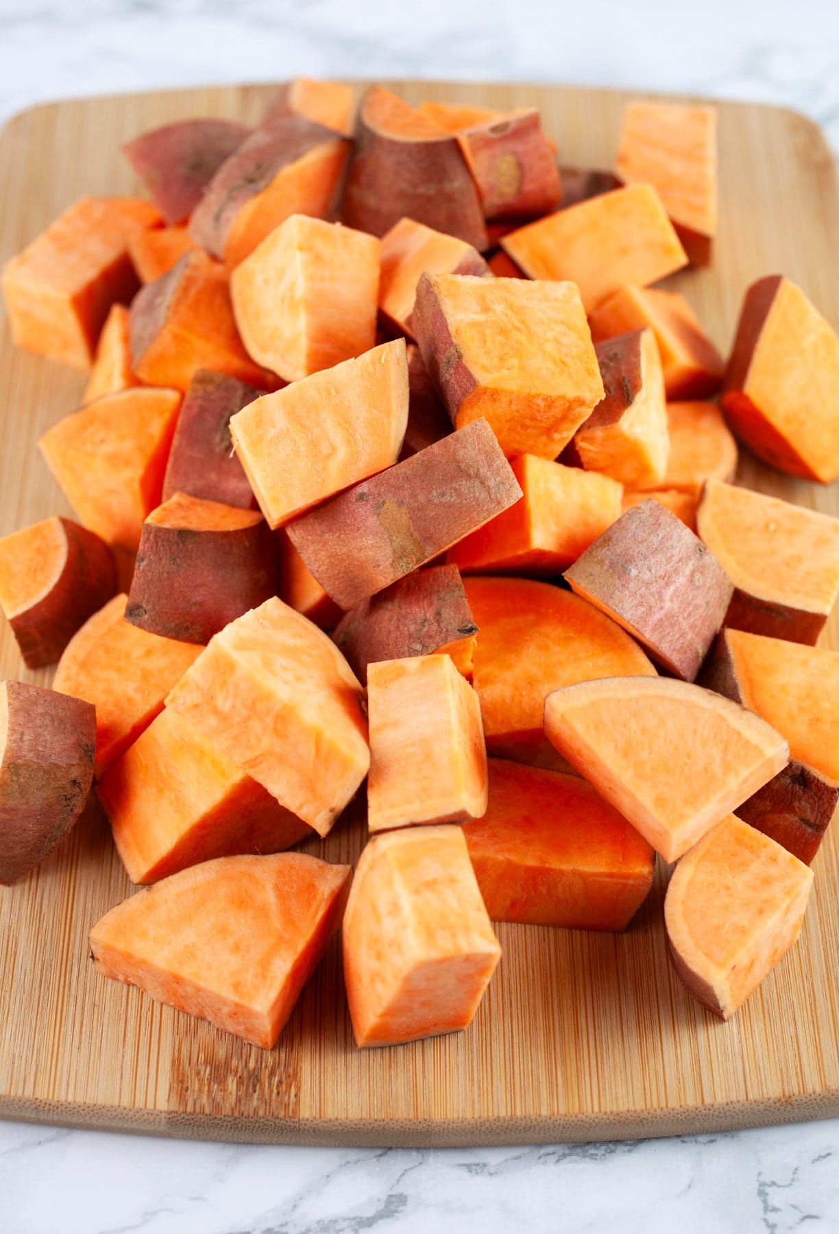 Chopped sweet potatoes on wooden cutting board.