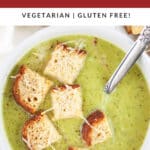 Asparagus broccoli soup with toasted Parmesan bread cubes in white bowl with spoon.