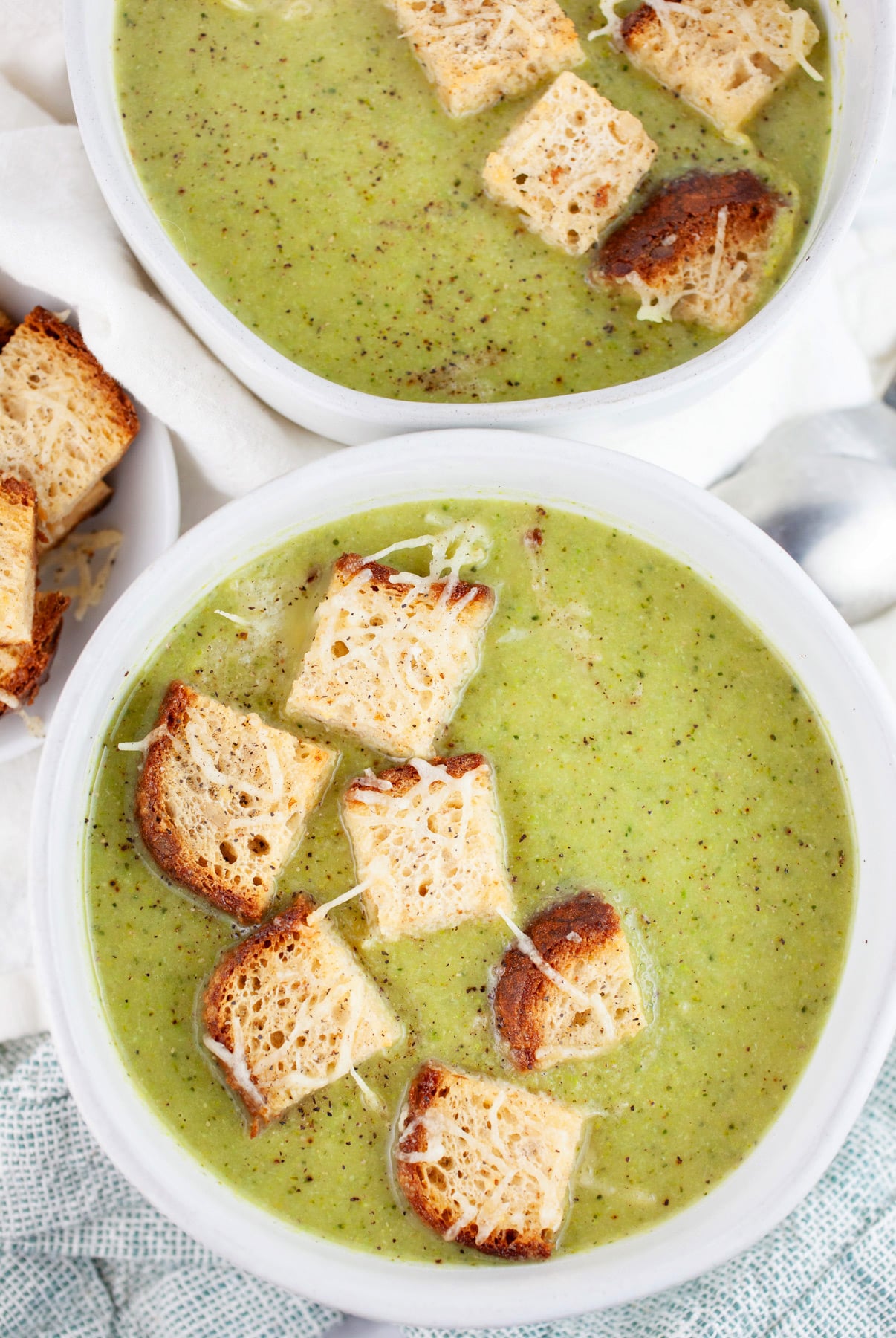 Broccoli asparagus soup with toasted Parmesan bread cubes in white bowls.