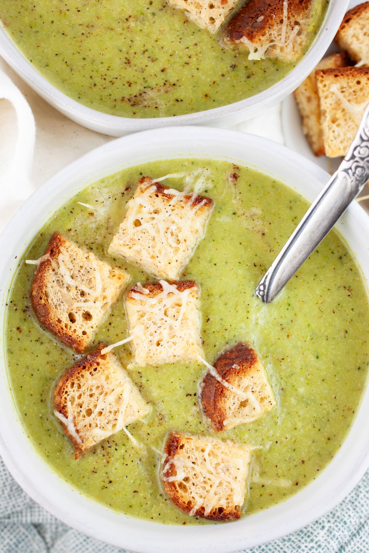 Asparagus broccoli soup with Parmesan croutons in white bowl with spoon.