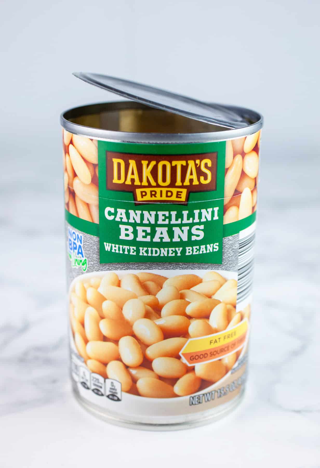 Opened can of cannellini beans on white surface.