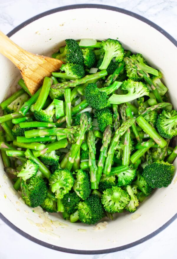 Asparagus and broccoli sauteed in Dutch oven with wooden spoon.