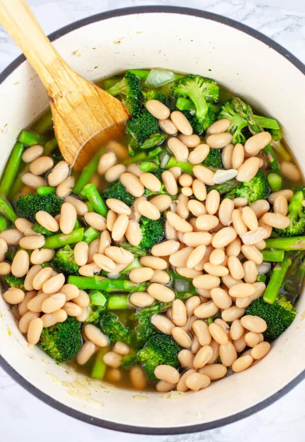 Broccoli asparagus soup with cannellini beans in Dutch oven with wooden spoon.