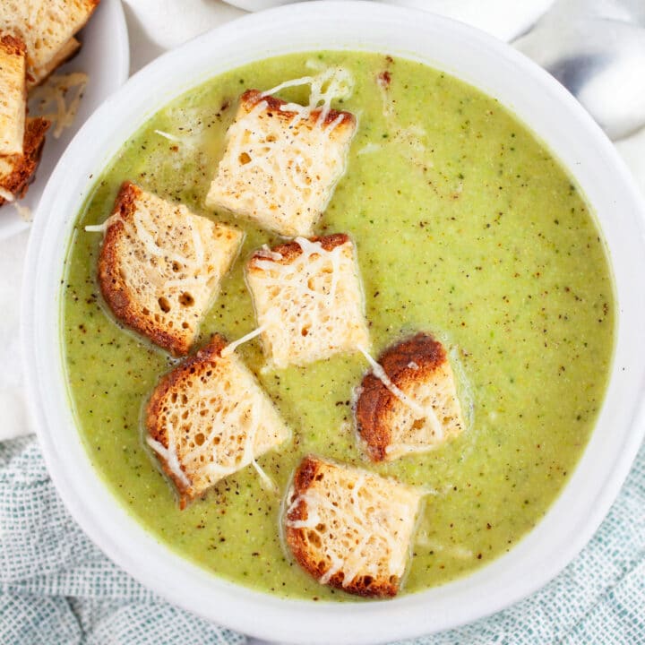 Broccoli asparagus soup with Parmesan croutons in white bowl.