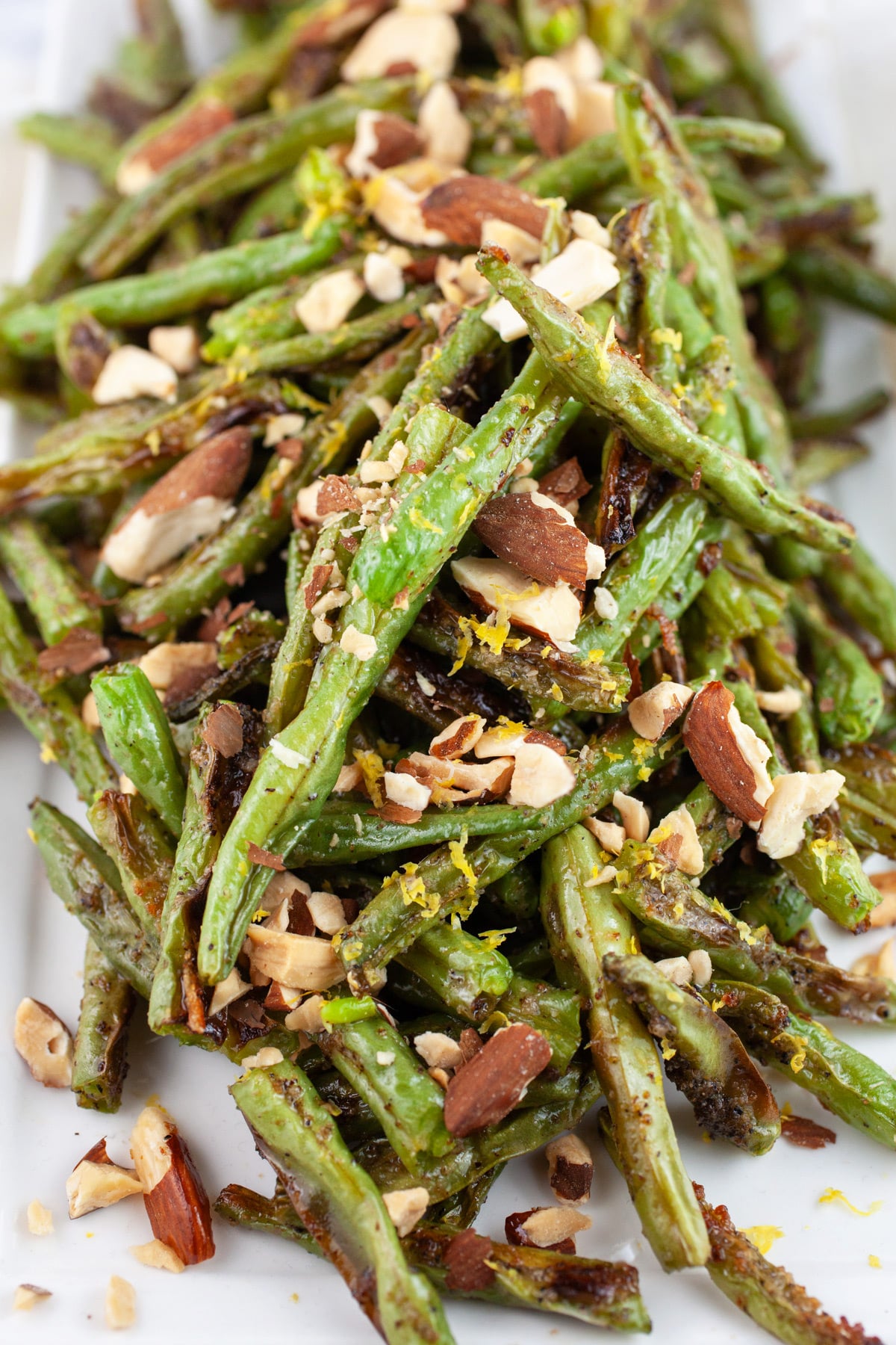 These Simple Garlicky Roasted Green Beans is one of the best easy and healthy side dishes out there! Fresh green beans are tossed in olive oil and garlic powder and then baked in the oven until nice and crispy and then topped with almonds. This quick vegetarian and vegan recipe is perfect for lunch or dinner! #greenbeans #vegetarian #vegan #garlic #withalmonds #easy Garlic roasted green beans with toasted almonds and lemon zest on white platter.