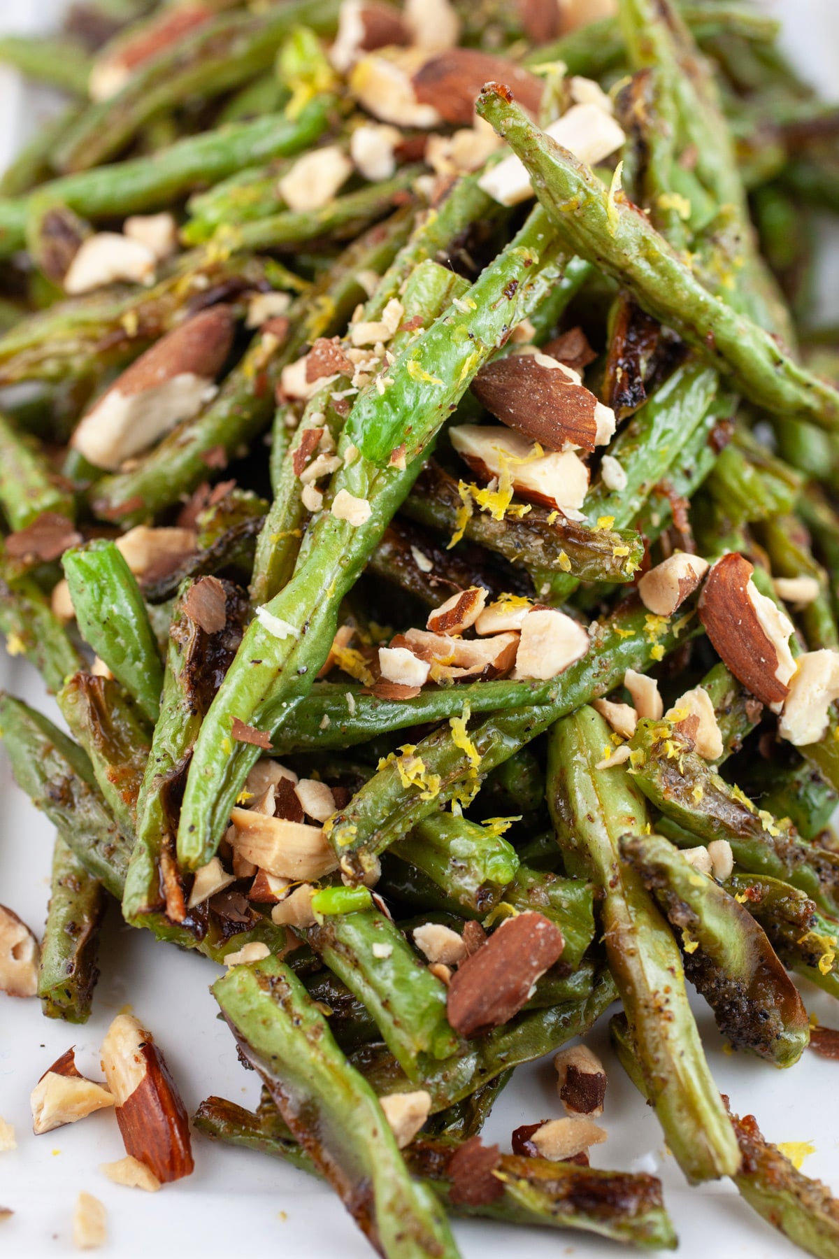 Roasted green beans with toasted almonds and lemon zest on white platter.