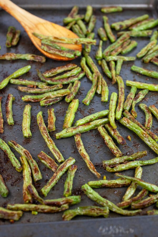Roasted green beans on baking sheet with wooden spoon.